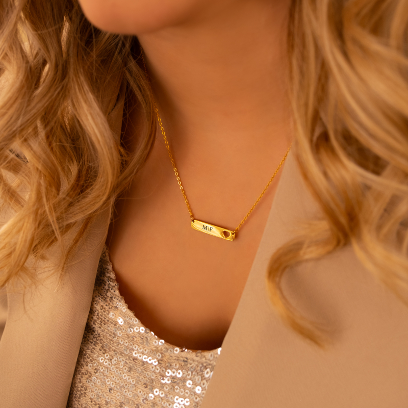 Model draagt een gouden graveerbare bar ketting met een hartje erin