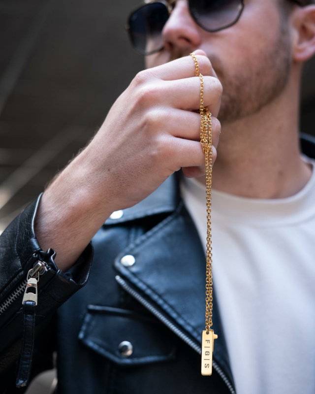 Man houdt stoere gouden ketting met gravering vast